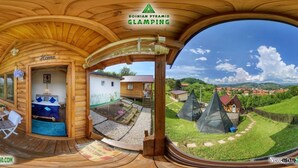 A wooden cabin with a covered porch, a small outdoor seating area, and a view of a village with pyramid-shaped structures. - Blue bungalow Bosnian pyramid glamping (Visoko)