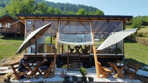A modern outdoor dining area with wooden furniture and a glass enclosure. - Blue bungalow Bosnian pyramid glamping (Visoko)