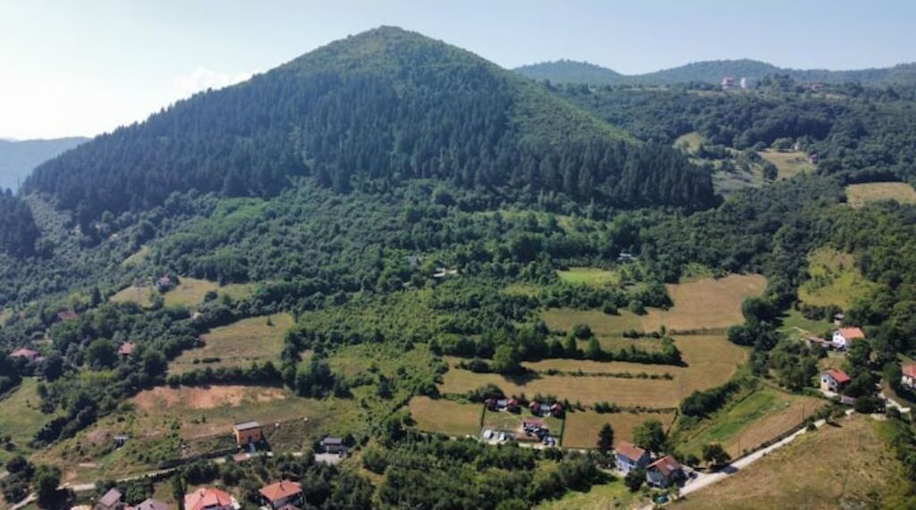 Un paysage rural avec une colline, des maisons éparpillées et des champs.