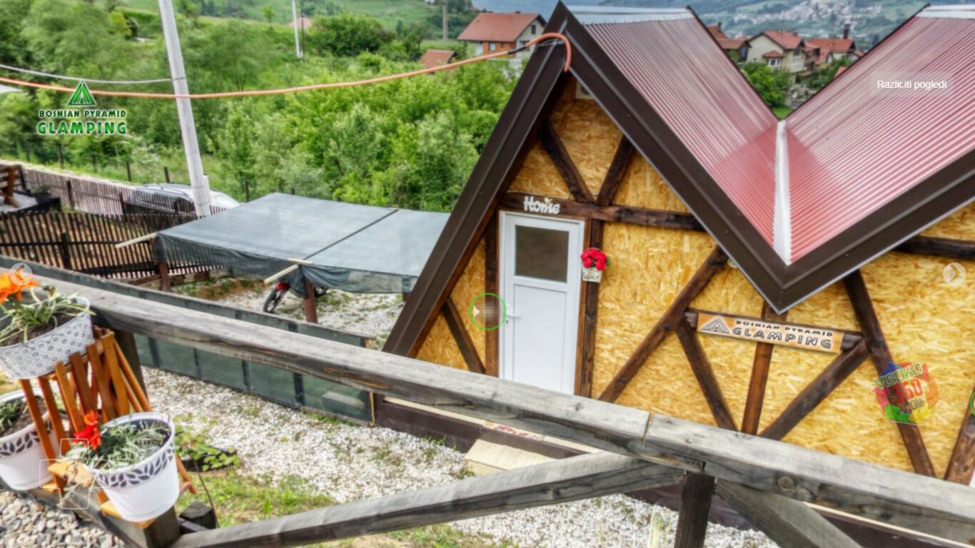 A wooden house with a sloped roof, a door, and a window. There is a sign on the house that reads "Bosnian Pyramid Glamping".