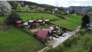 A rural setting with several wooden cabins, a large barn, and a paved driveway. - Red bungalow Bosnian pyramid glamping (Visoko)