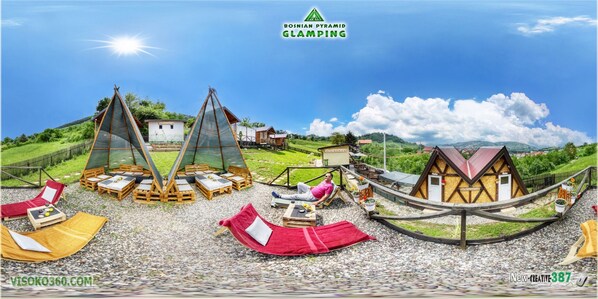 A glamping site with wooden structures, outdoor seating, and a scenic view.