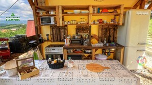 A compact kitchen with wooden shelves, a microwave, a refrigerator, and a table with a patterned tablecloth. - Green bungalow Bosnian pyramid glamping (Visoko)