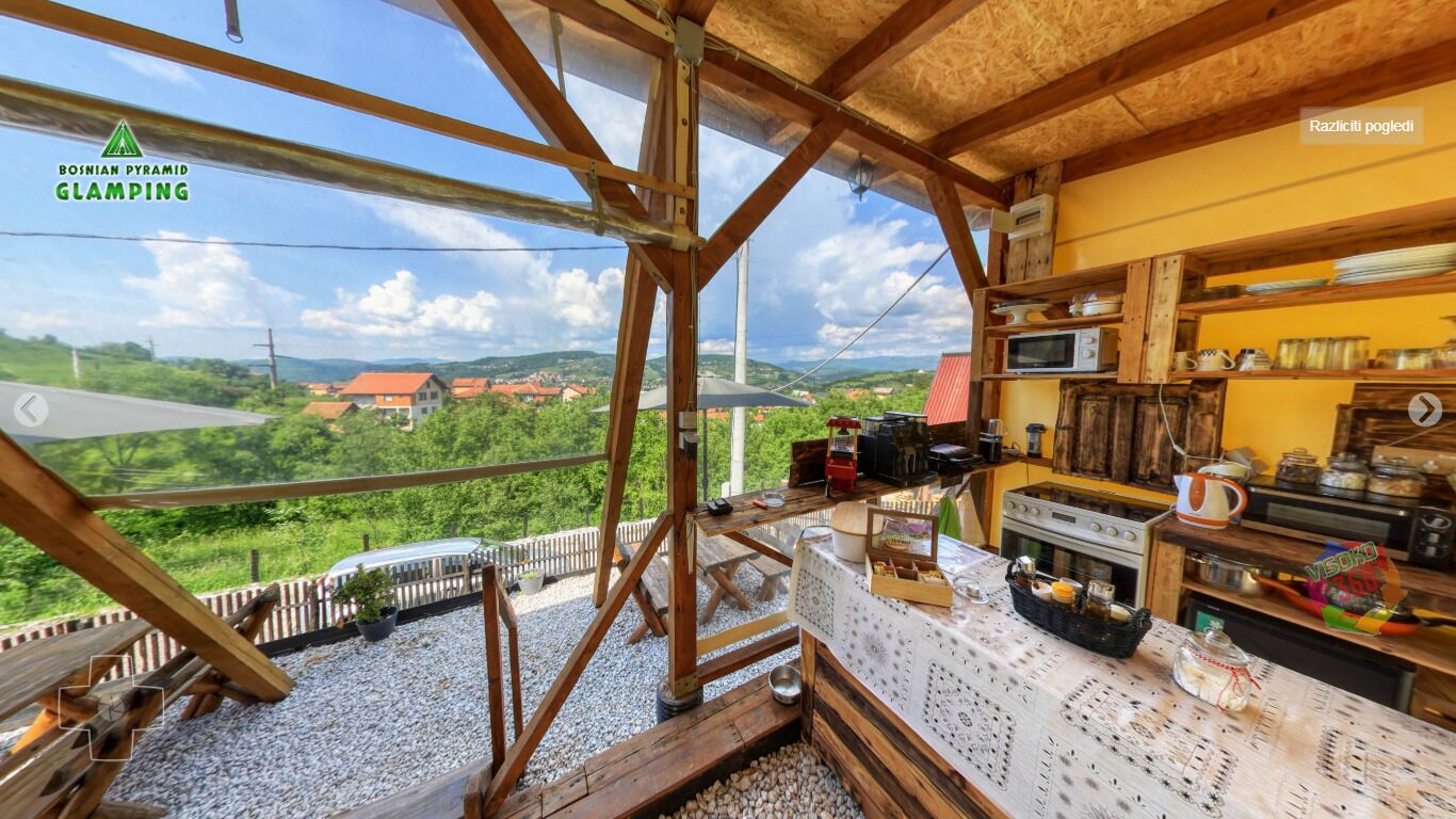 A rustic kitchen with a view of a village, wooden beams, and a table with food items.