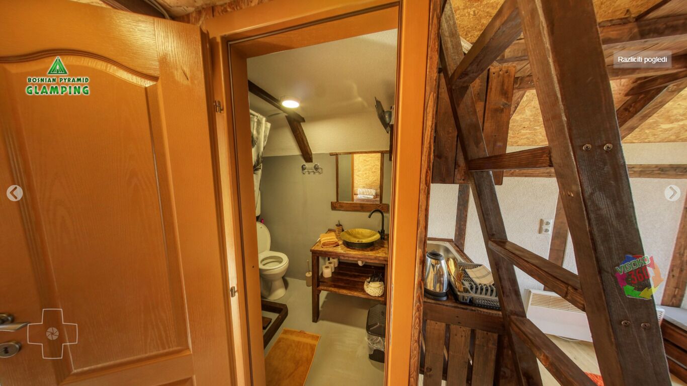 Une porte en bois rustique ornée d’un logo, une échelle en bois et une salle de bain équipée de toilettes, d’un lavabo et d’étagères en bois.