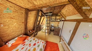 A wooden interior with a bed, a small kitchenette, and a ladder leading to a loft area.