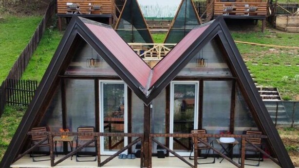 A modern, triangular-shaped building with large windows and a dining area on the ground floor.