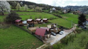 A rural setting with several wooden cabins, a large barn, and a car parked near the entrance.