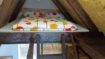 A loft-style bedroom with a sloped ceiling, wooden beams, and a ladder leading to a lower level.