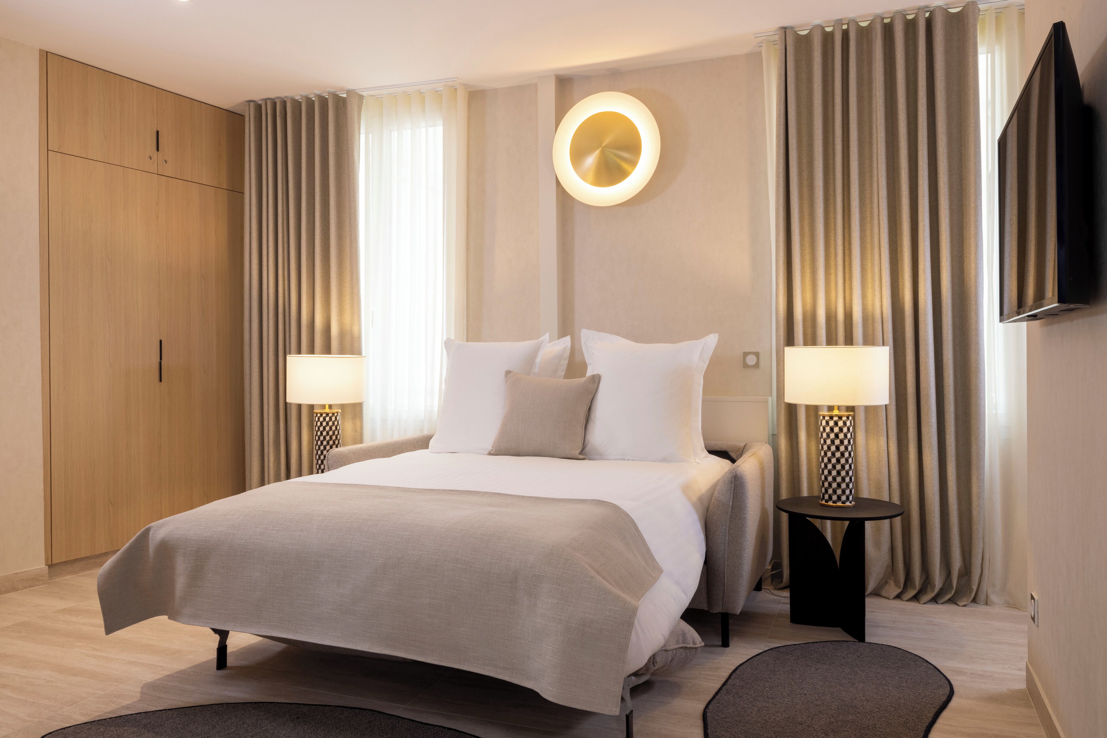 Una habitación de hotel con una cama grande, dos mesitas de noche con lámparas, un televisor montado en la pared y un armario de madera.