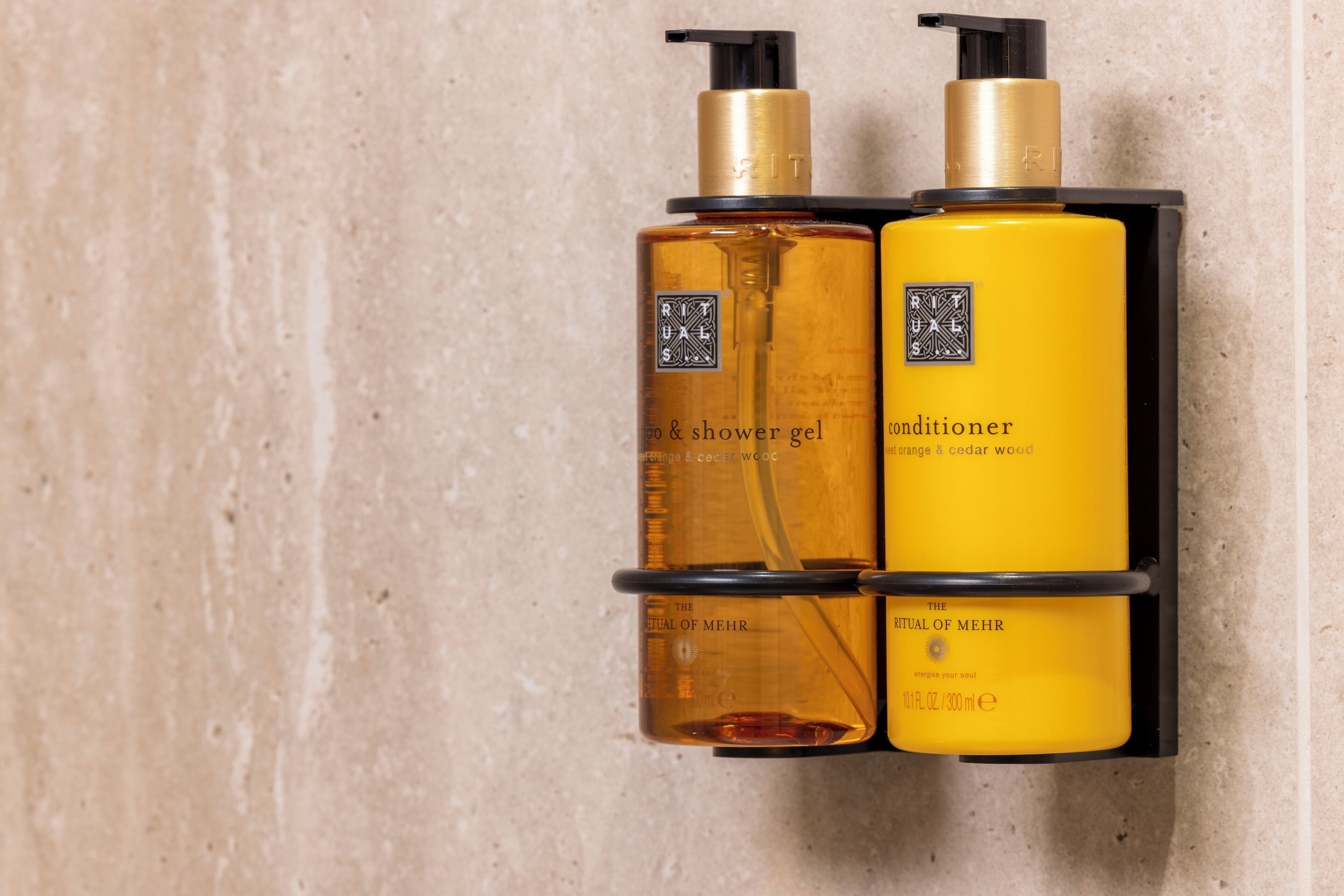 Dois frascos dos produtos The Ritual of Meer, um gel de banho e um condicionador, fixados numa parede preta.