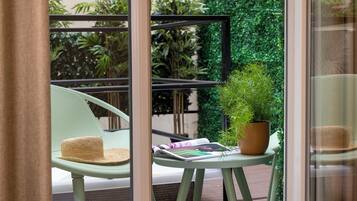 A balcony with a green chair, a small table with a potted plant, and a magazine.