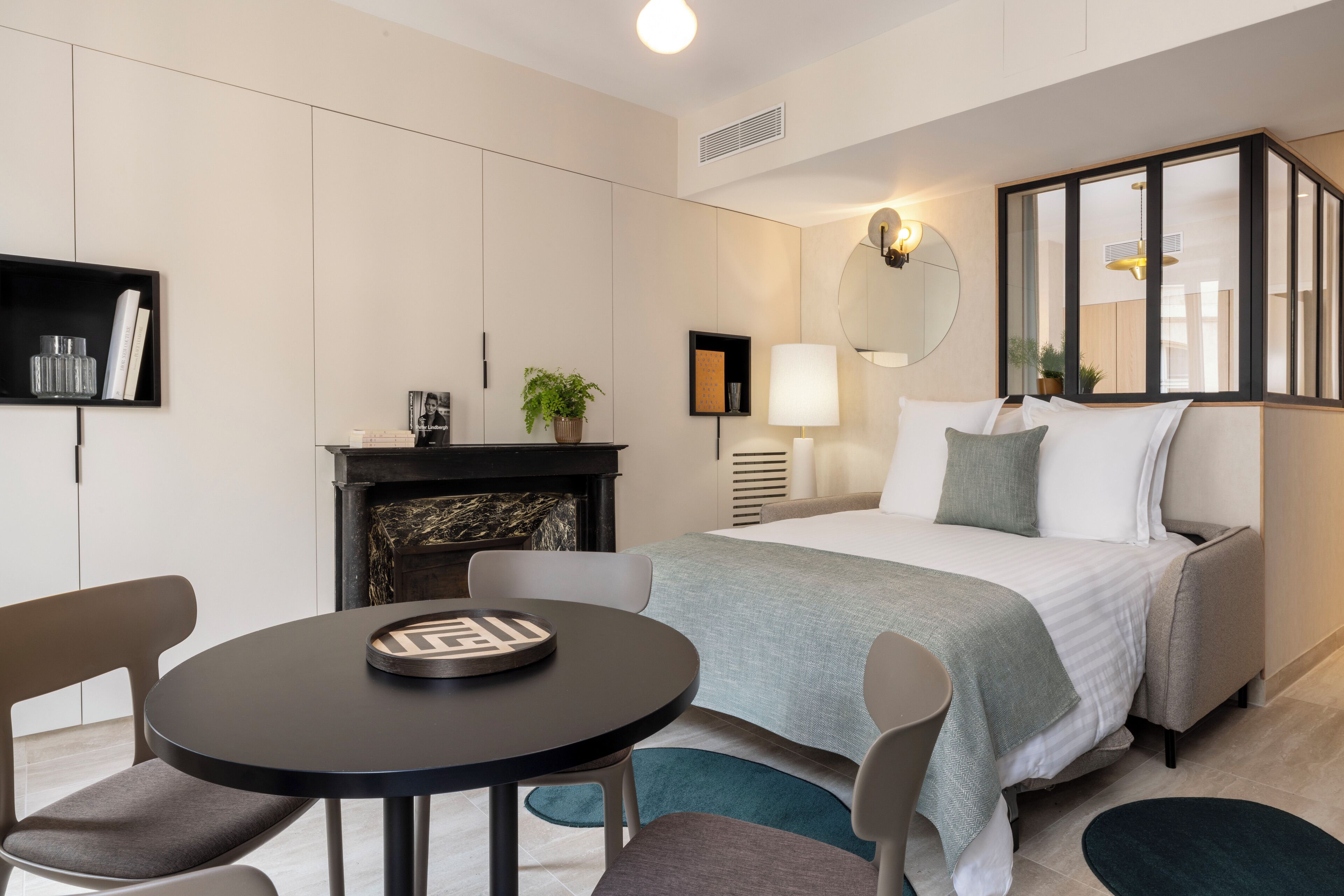 A modern hotel room with a bed, a round table, and a fireplace.