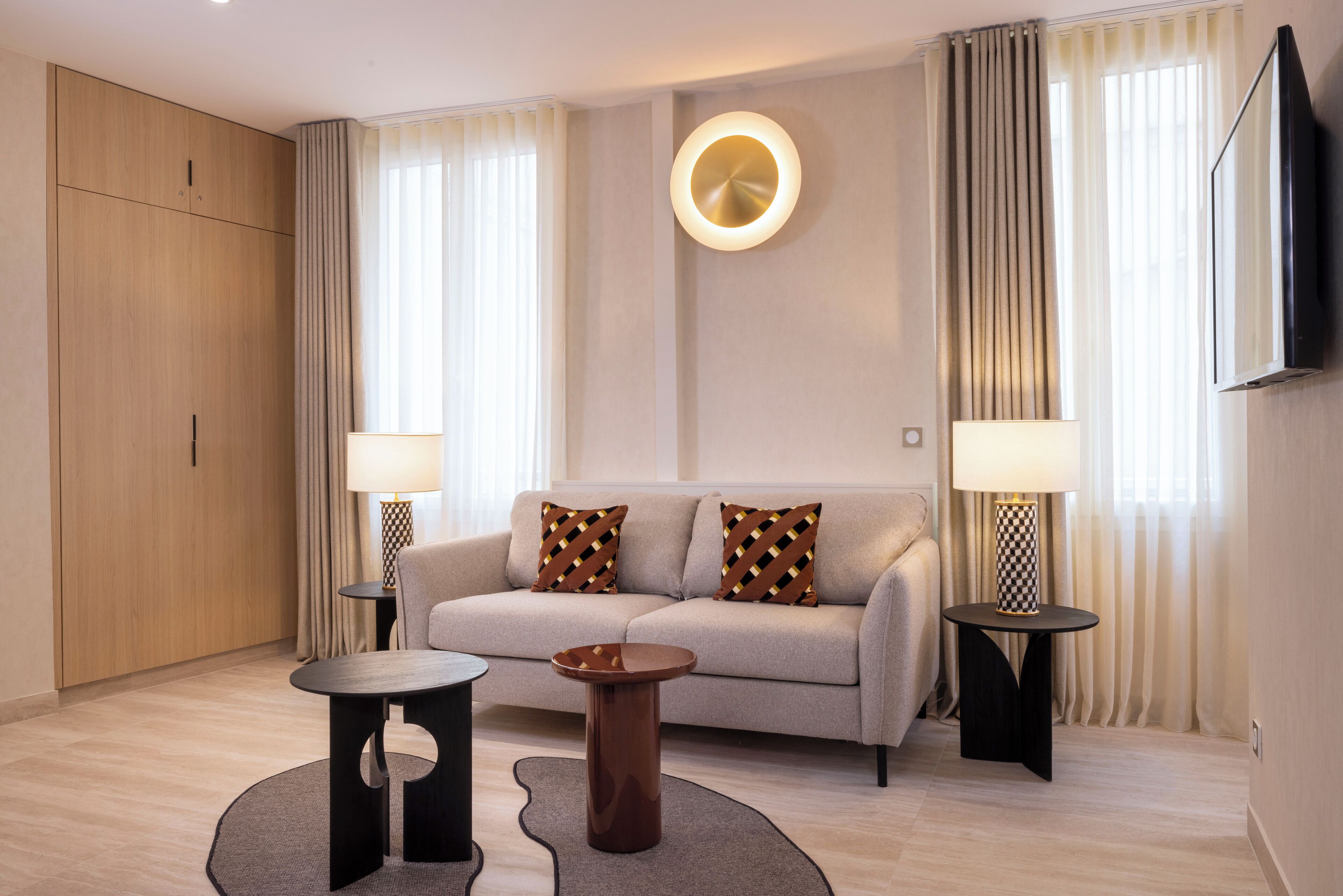 A modern living room with a sofa, two side tables, a round coffee table, and a wall-mounted TV.