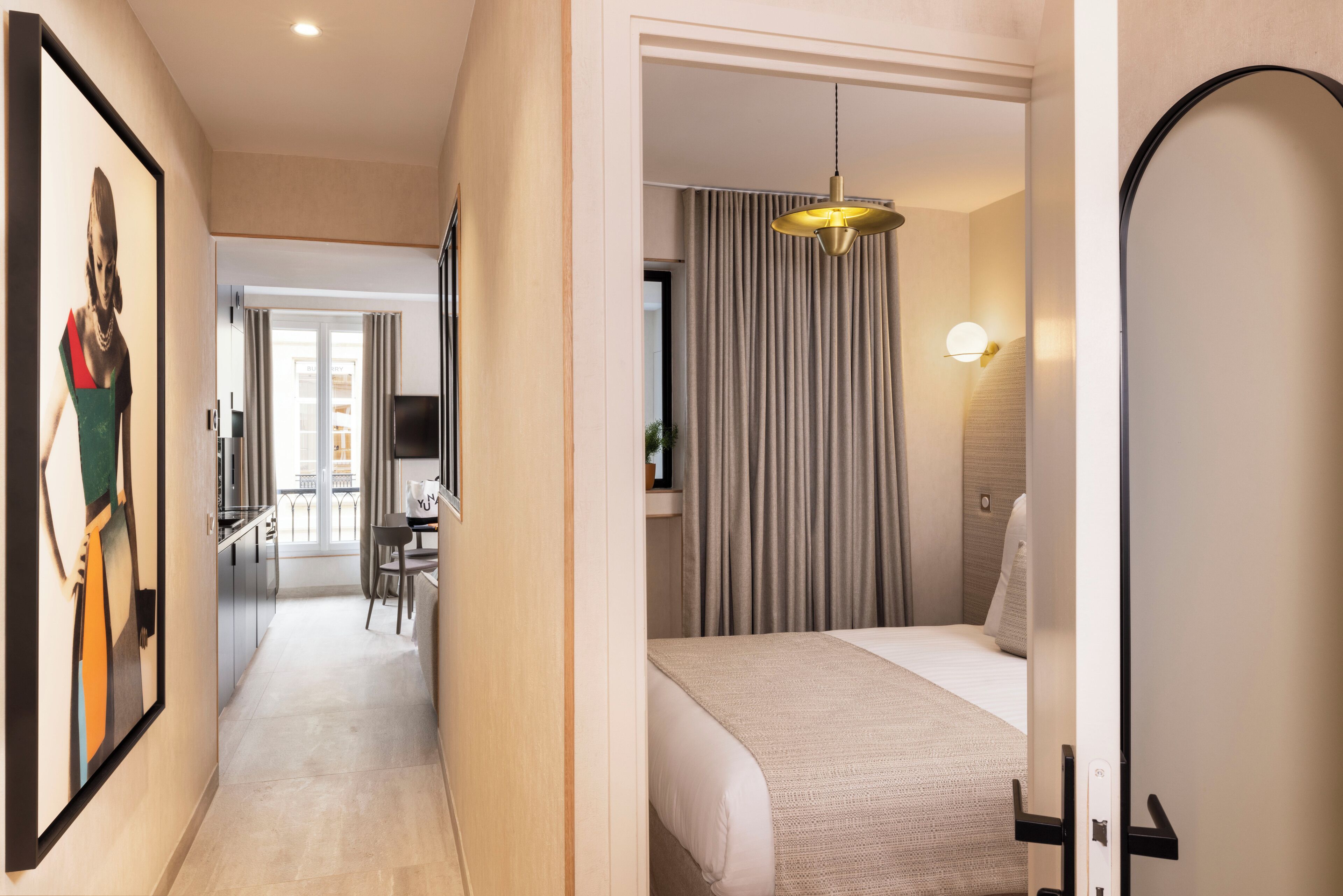 Ein Hotelzimmer mit Bett, Nachttisch, Lampe und Blick auf den Flur.