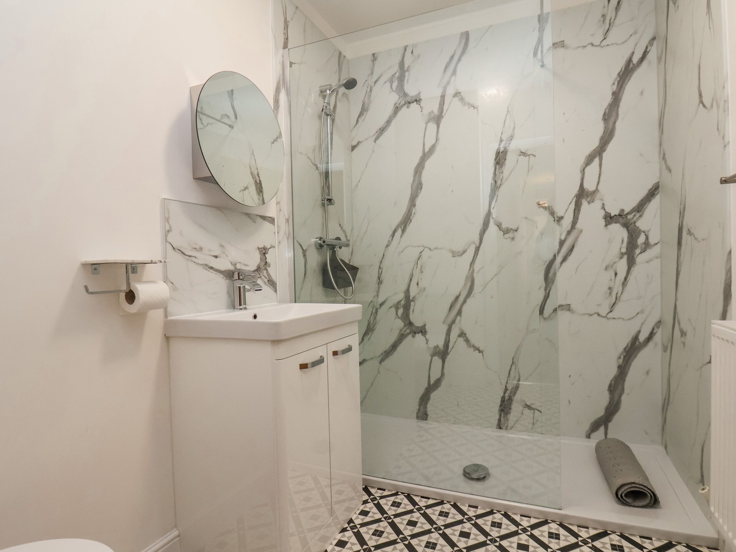 A bathroom with a marble shower, a sink, and a toilet.