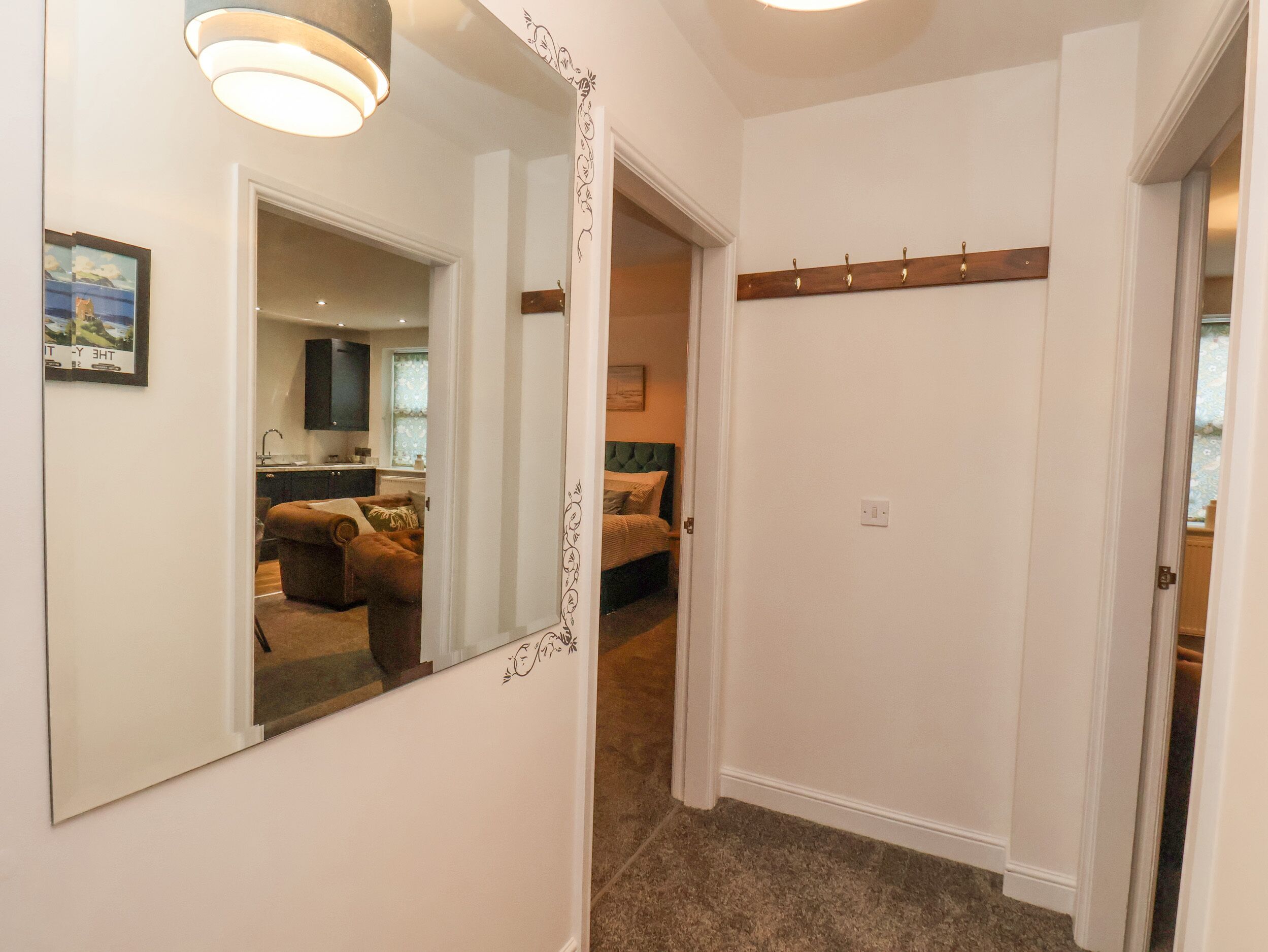 A hallway with a mirror, a door with a wooden handle, and a small window with a view of a room.