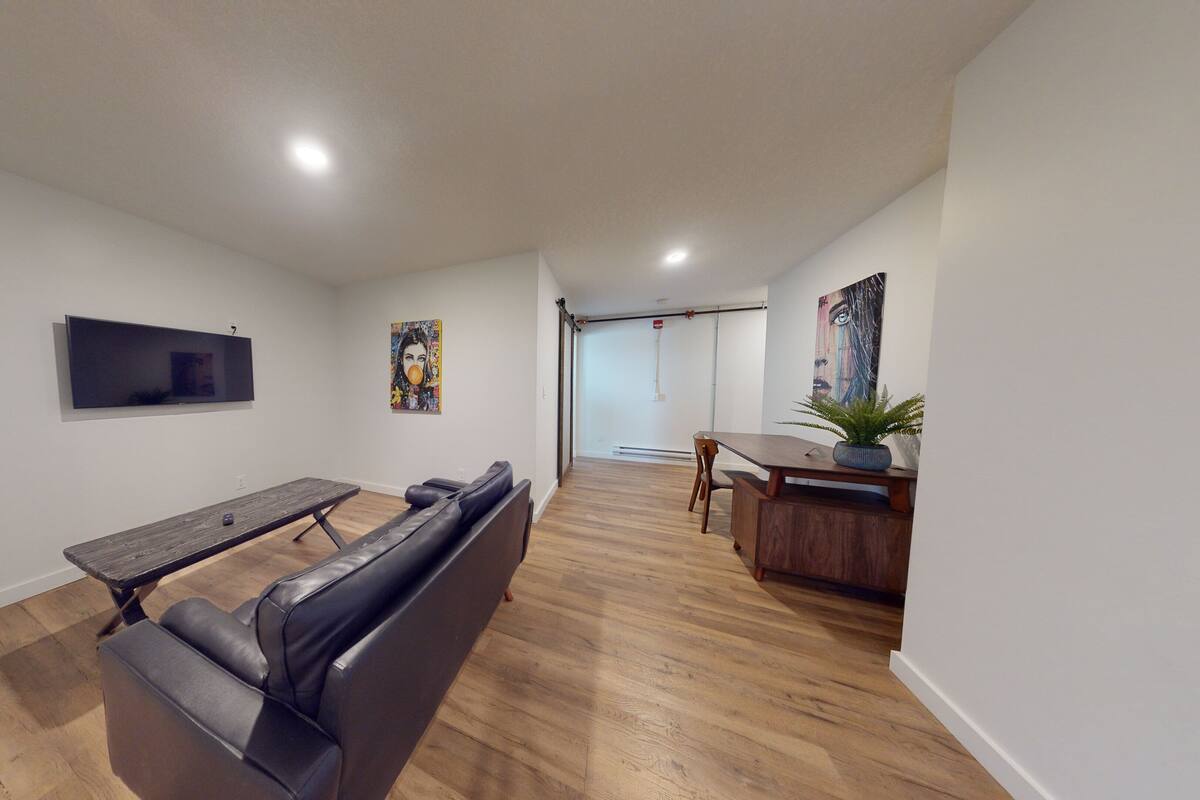 A spacious living area with a sofa, a dining table, and a TV mounted on the wall.