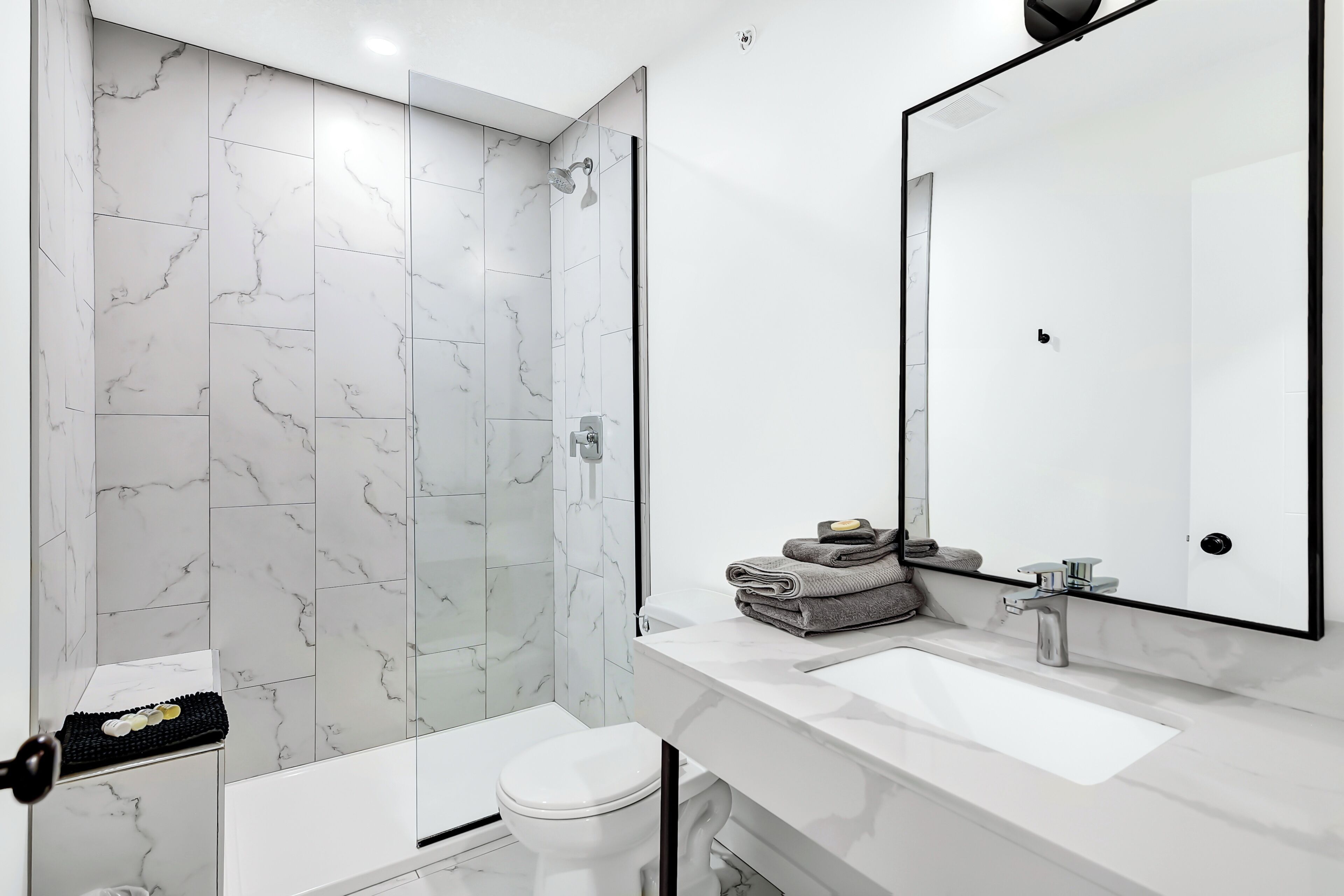 A modern bathroom with a white marble shower, a white toilet, and a vanity with a large mirror and sink.