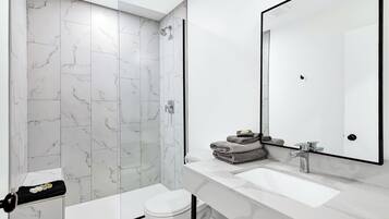 A modern bathroom with a white marble shower, a white toilet, and a vanity with a large mirror and sink.
