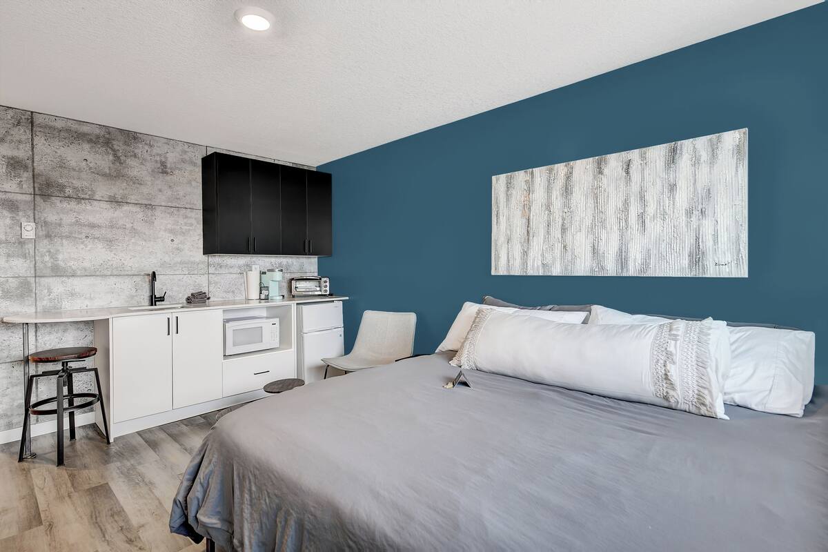 A modern bedroom with a bed, a desk, and a kitchenette.
