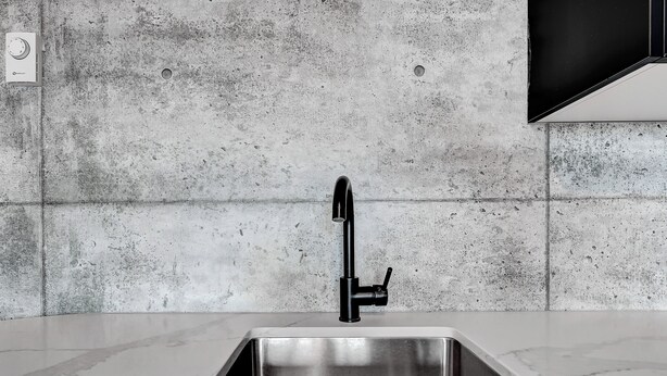 Una cocina moderna con un lavamanos de acero inoxidable, un grifo negro y un salpicadero de hormigón.