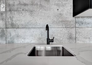 A modern kitchen with a stainless steel sink, a black faucet, and a concrete backsplash. - RNDUP  (Clairmont)
