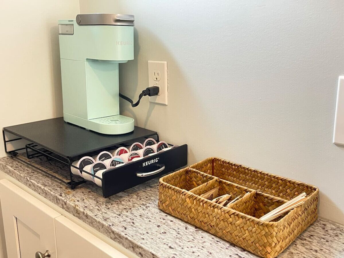 Eine Kaffeemaschine auf einer Arbeitsplatte, eine Schublade mit Kaffeekapseln und ein gewebter Korb.