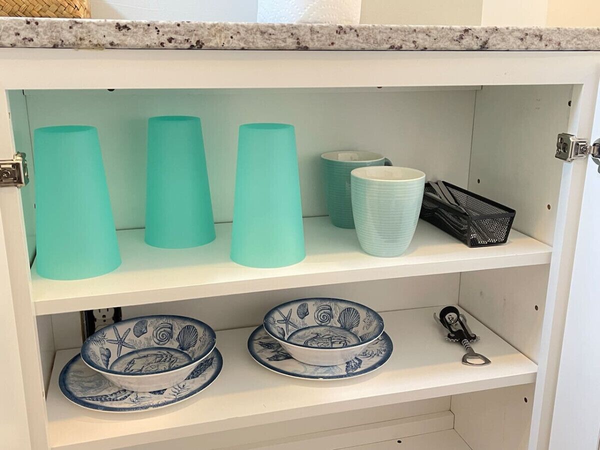 A kitchen cabinet with teal-colored cups, a white bowl, and a black basket.