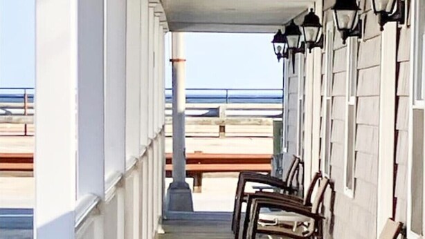 Area esterna coperta con sedute e tavoli in legno, affacciata su una spiaggia.