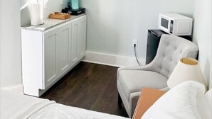 Una stanza compatta con un letto, un angolo cottura attrezzato con forno a microonde, macchina del caffè e una sedia.
