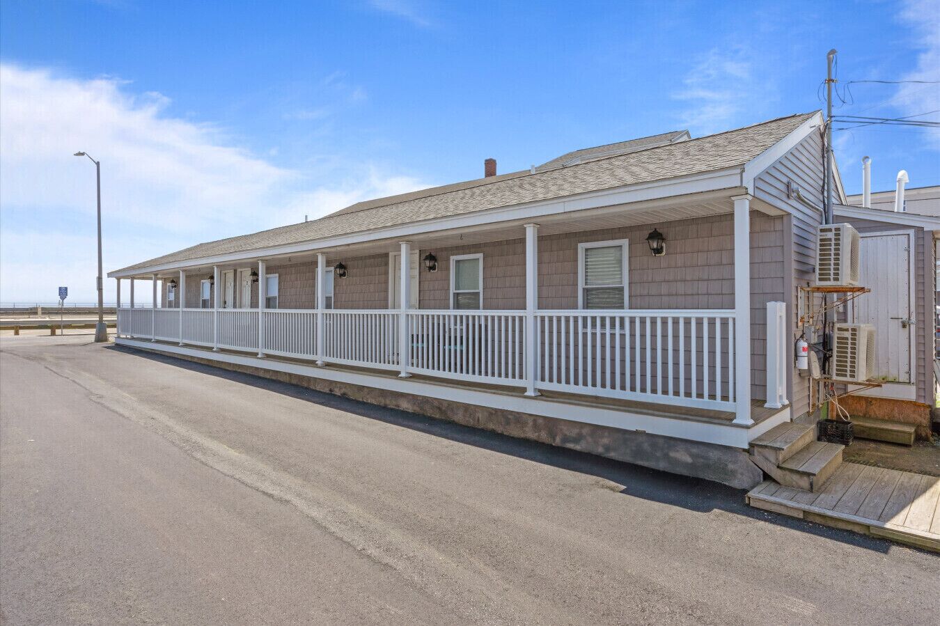 A coastal building with a covered porch, air conditioning units, and a small staircase leading to the entrance.