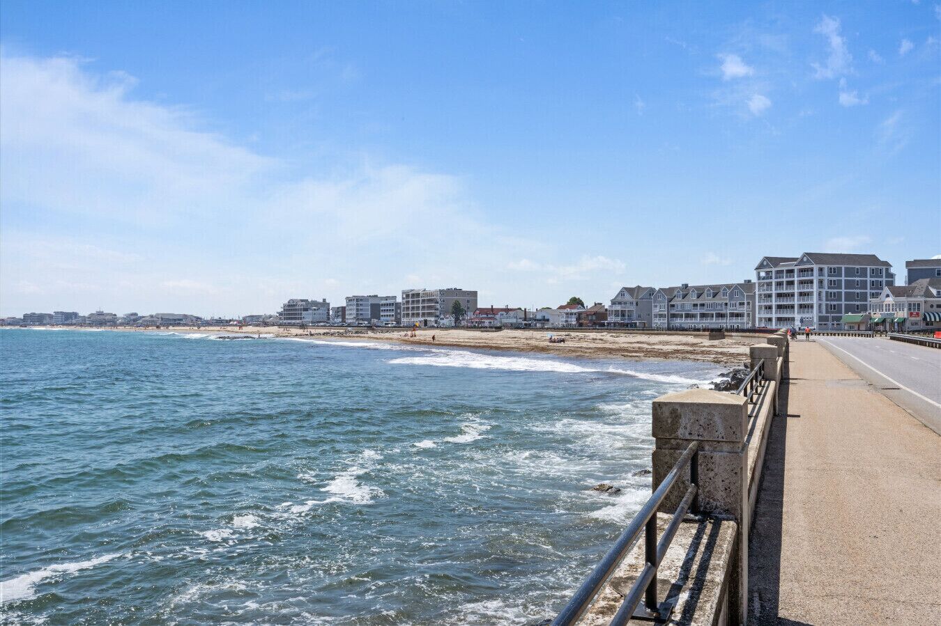A coastal road with a beach on one side and buildings in the background.