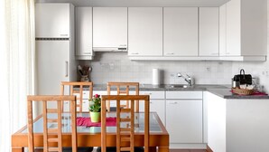 Une cuisine moderne avec des meubles blancs, une table à manger en verre et une plante en pot.