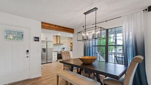 A modern kitchen with a dining area, featuring a large window, wooden flooring, and a central island with a bowl.