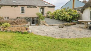 A stone house with a garden patio, a small table, and a variety of plants. - Gilly Skyber (Helston)