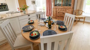 A modern kitchen with white cabinets, a wooden dining table set for six, and a traditional wooden cabinet with glass doors. - Gilly Skyber (Helston)