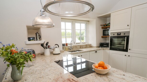 A modern kitchen with granite countertops, a built-in oven, and a window providing natural light. - Gilly Skyber (Helston)