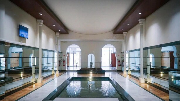 Amplia zona de piscina interior con una fuente central, grandes ventanales y un diseño arquitectónico moderno.