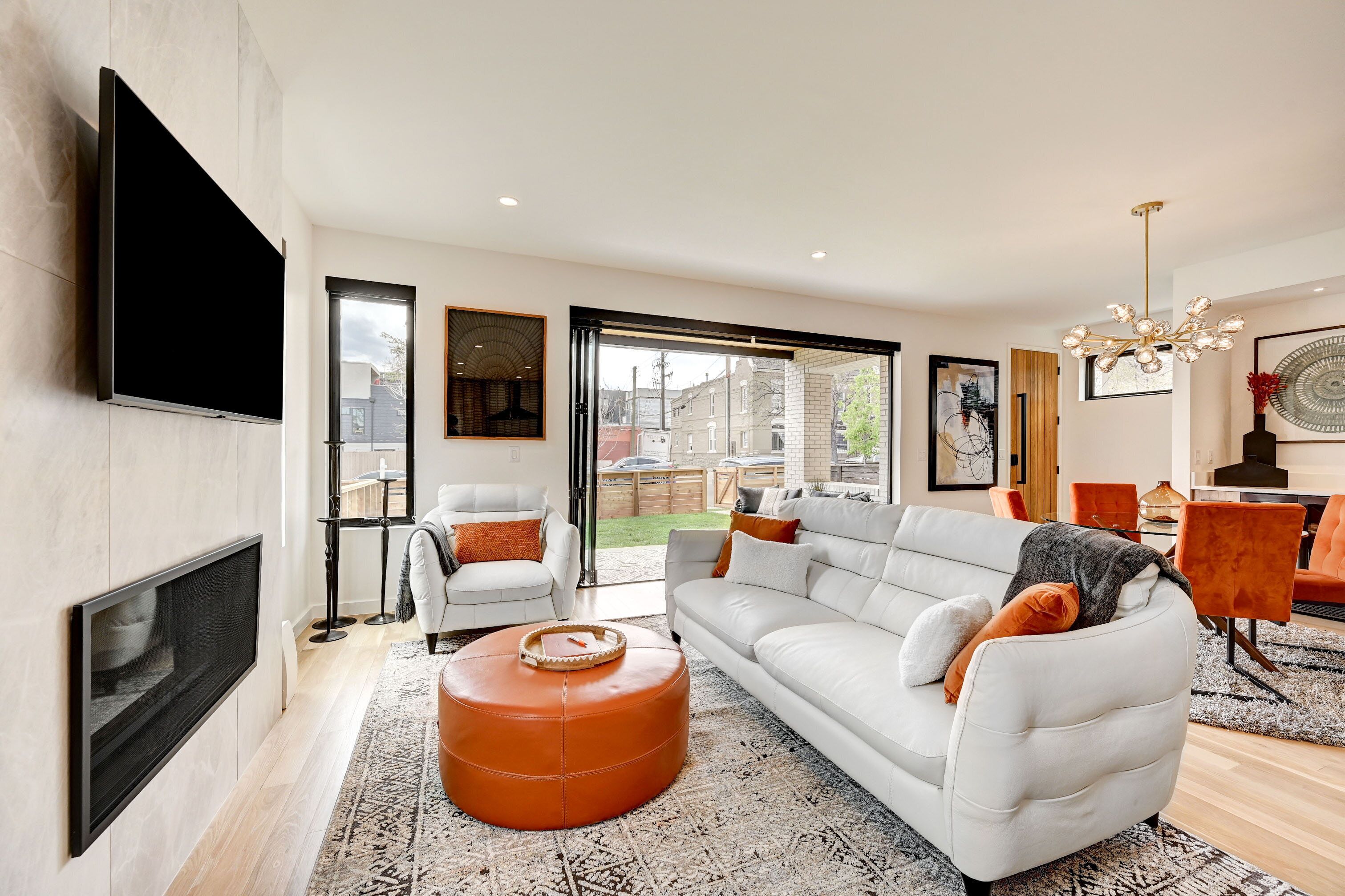 Un salon moderne avec un canapé blanc, un pouf en cuir et un téléviseur à écran plat fixé au mur.