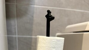 Ein Toilettenpapierhalter mit ungewöhnlichem Design, platziert in einem Badezimmer mit gefliesten Wänden.
