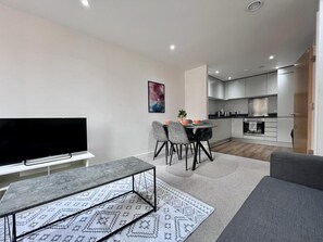 Un salon moderne avec un téléviseur à écran plat, un canapé gris et un tapis à motifs.