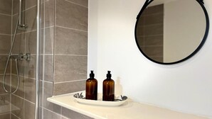 Ein Badezimmer mit Dusche, einem Waschbecken mit zwei Flaschen und einem runden Spiegel.