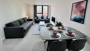 Ein modernes Wohnzimmer mit einer Sofagarnitur, einem Esstisch mit Schalen und einem großen Fenster mit Blick auf die Stadt.