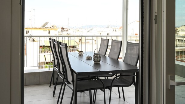 Un balcone con tavolo e sedie, vista sulla città e una porta che dà all'interno.