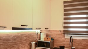 Una cucina moderna con mobili bianchi, un piano di lavoro in legno, forno integrato, microonde e lavello in acciaio inossidabile.