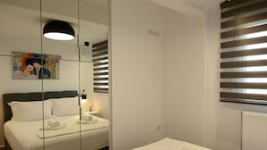 Una camera d'albergo con un letto, un comodino con una lampada, un quadro appeso al muro e una finestra con persiane.