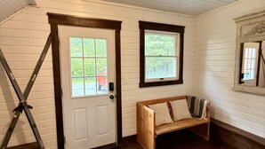 A room with a white door, a window, a wooden bench, and a black mat.