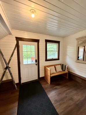 A room with a white door, a window, a wooden bench, and a black mat.