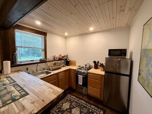 A compact kitchen with wooden cabinets, a stainless steel refrigerator, a stove, and a microwave.